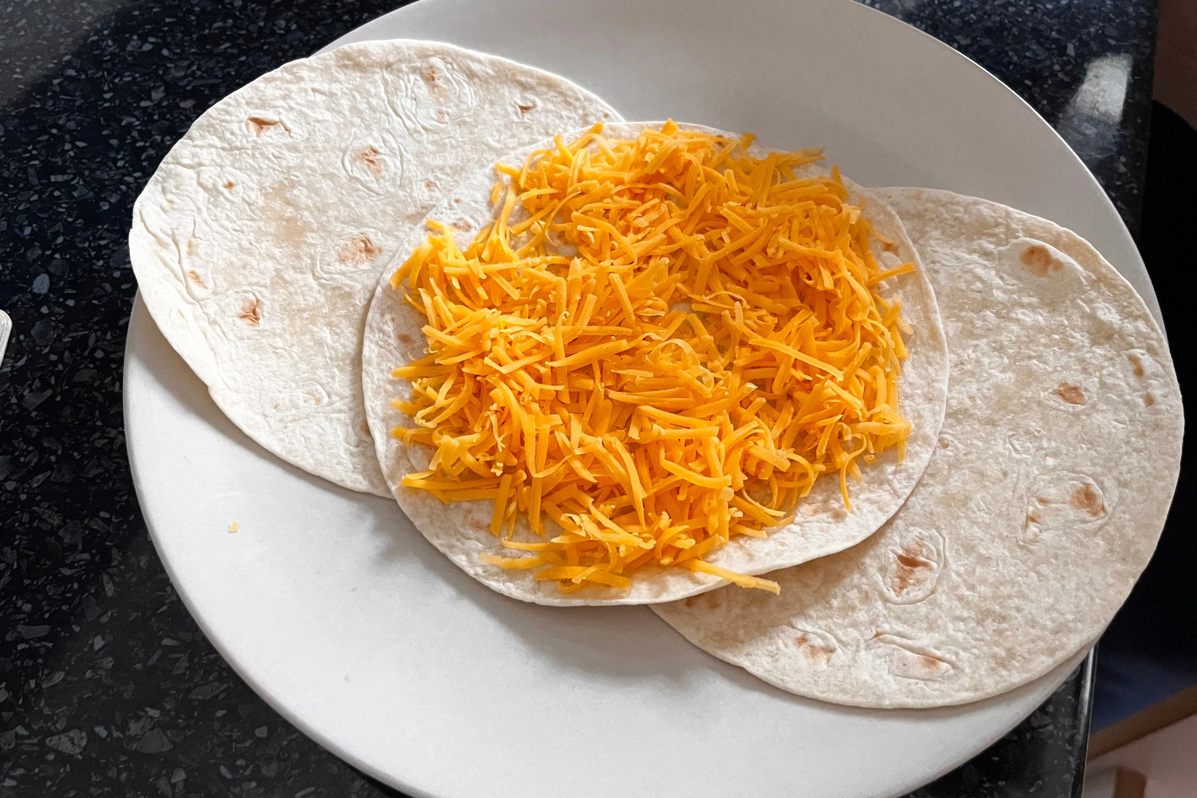 Grated Cheddar placed on a small wheat-flour tortilla before the quesadilla is closed