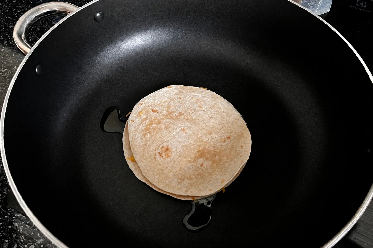 One assembled cheese quesadilla cooking in a large non-stick frying pan
