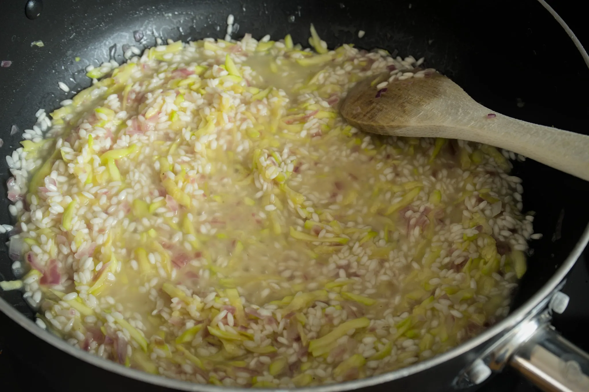 Zucchini risotto cooking with hot stock in a wide pan