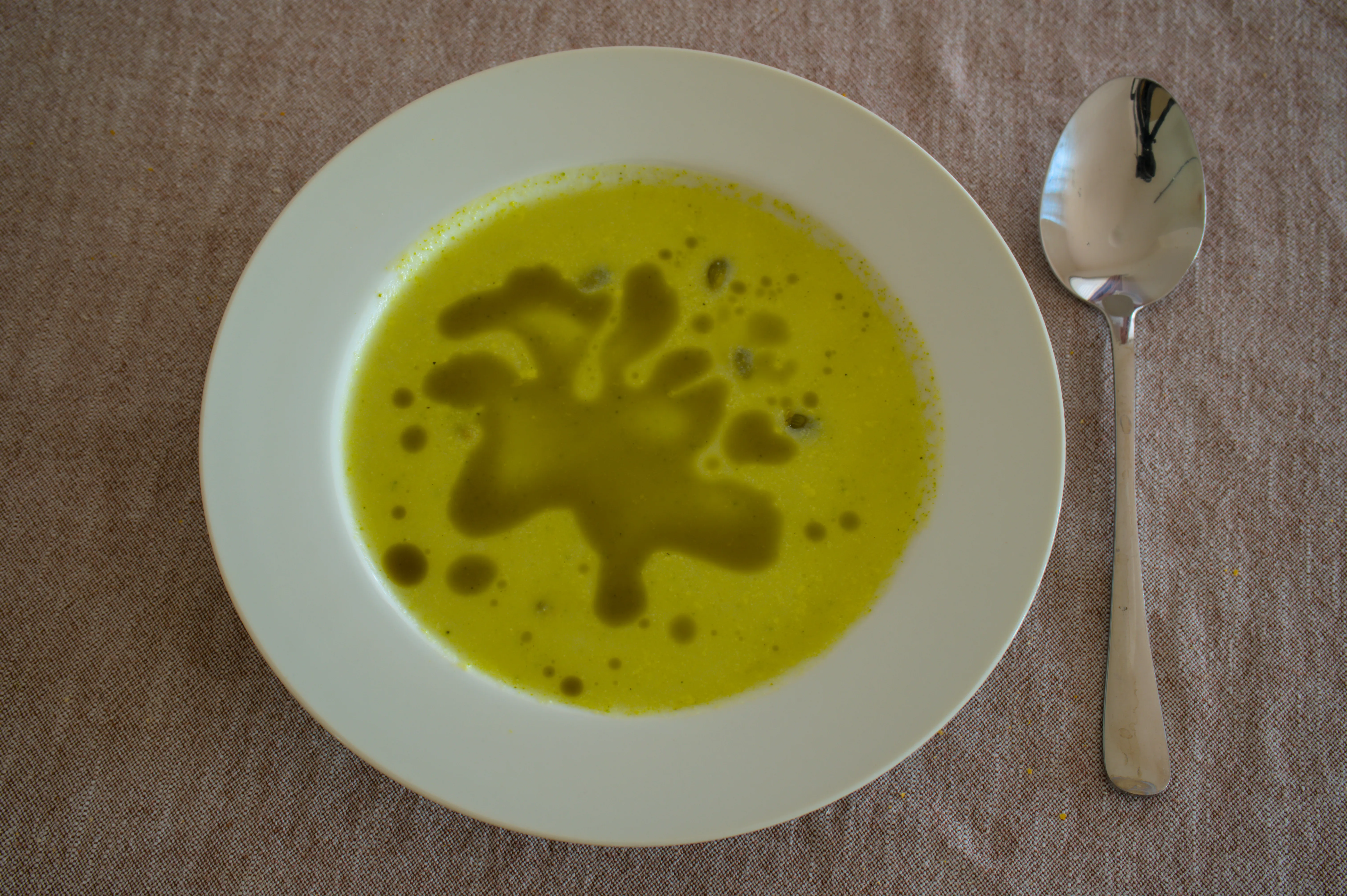 Creamy broccoli soup in a white bowl beside a spoon
