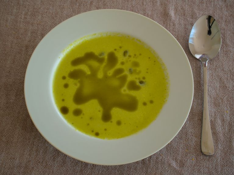Creamy broccoli soup in a white bowl beside a spoon