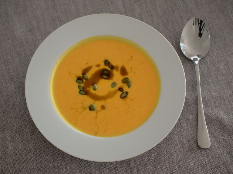 Creamy carrot soup topped with pumpkin seeds and pumpkin seed oil in a white bowl