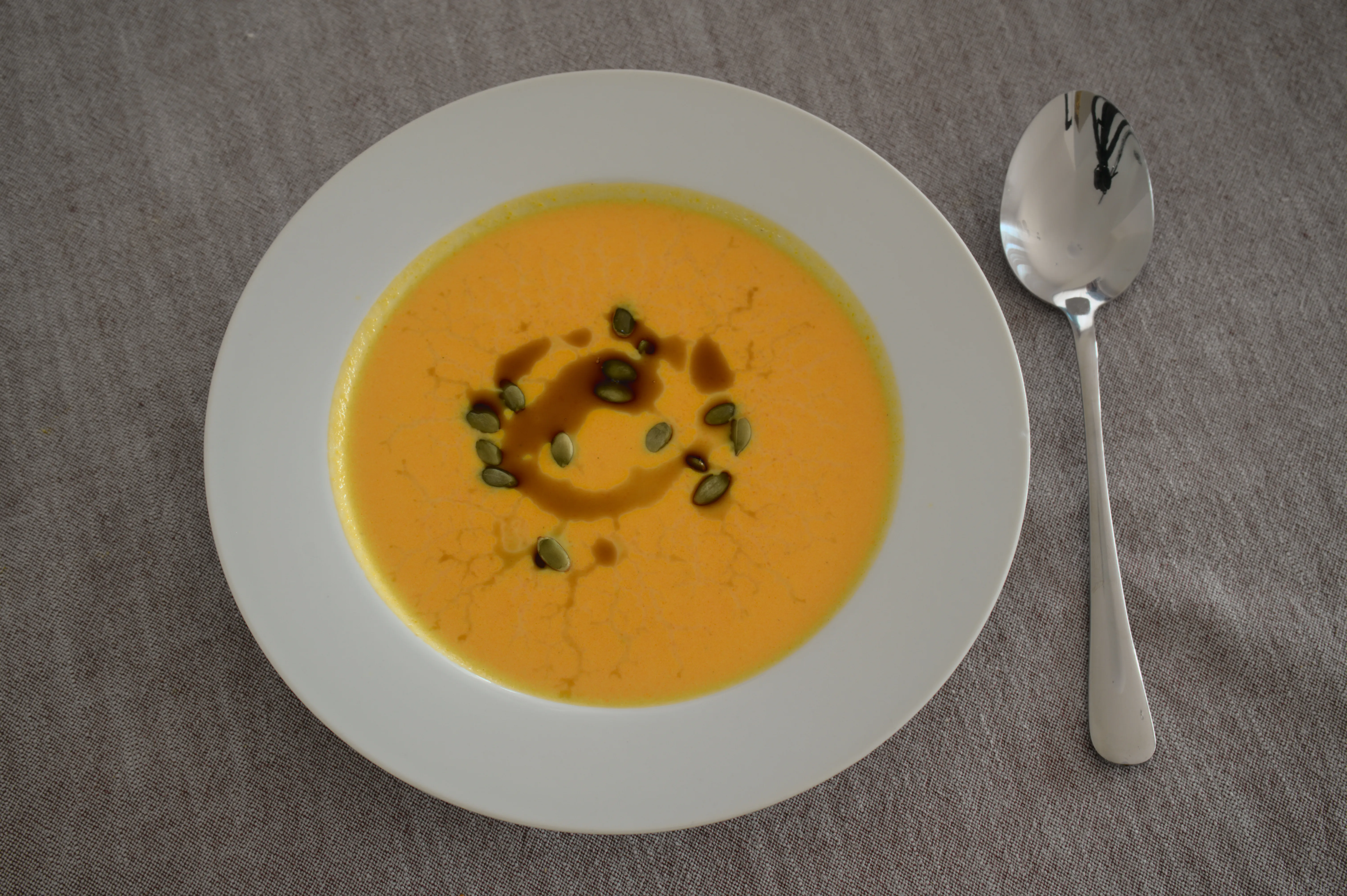 Cremige Karottensuppe mit Kürbiskernen und Kürbiskernöl in einer weißen Schale