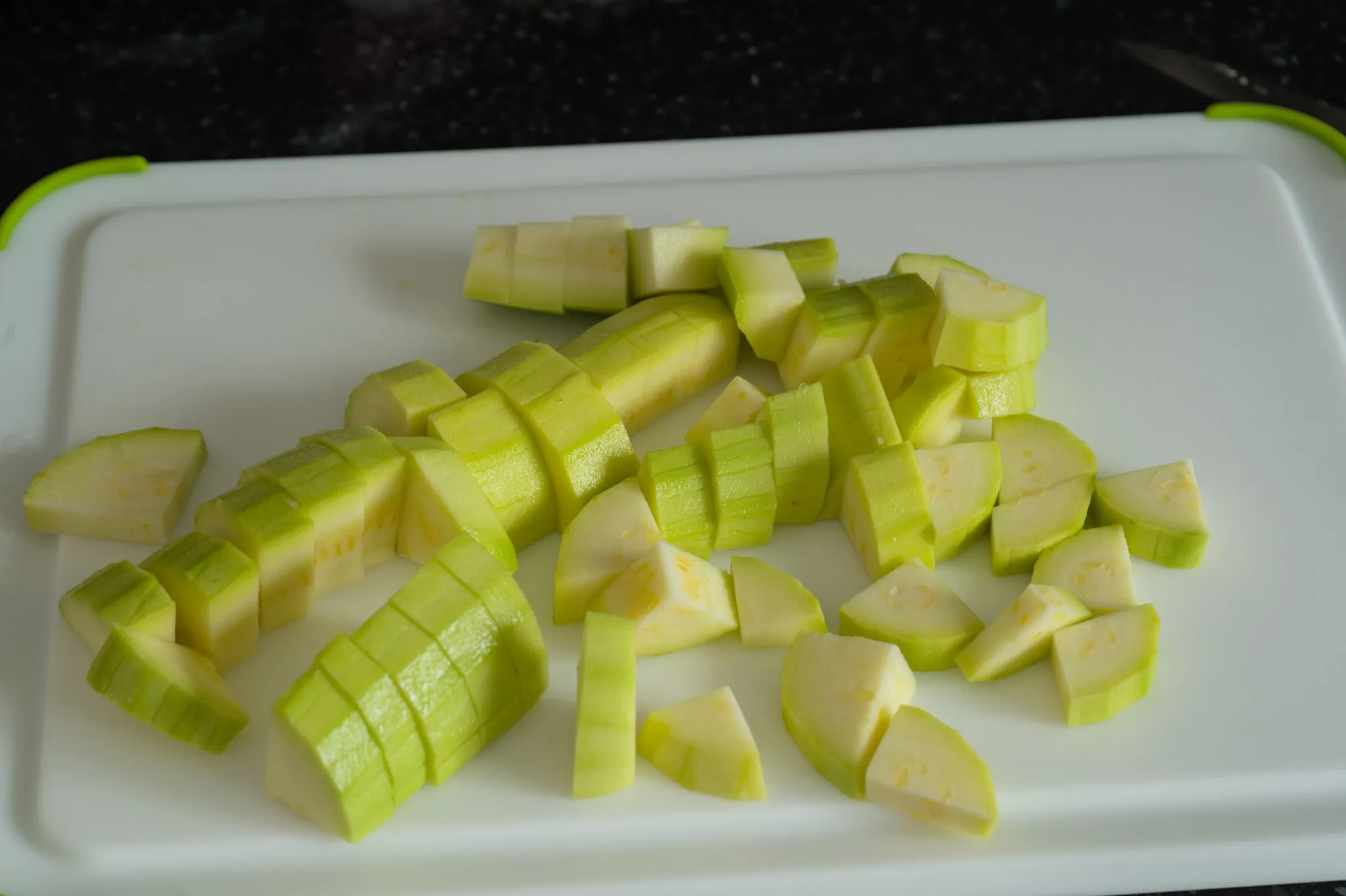 Peeled zucchini cut into small pieces on a cutting board for browning separately