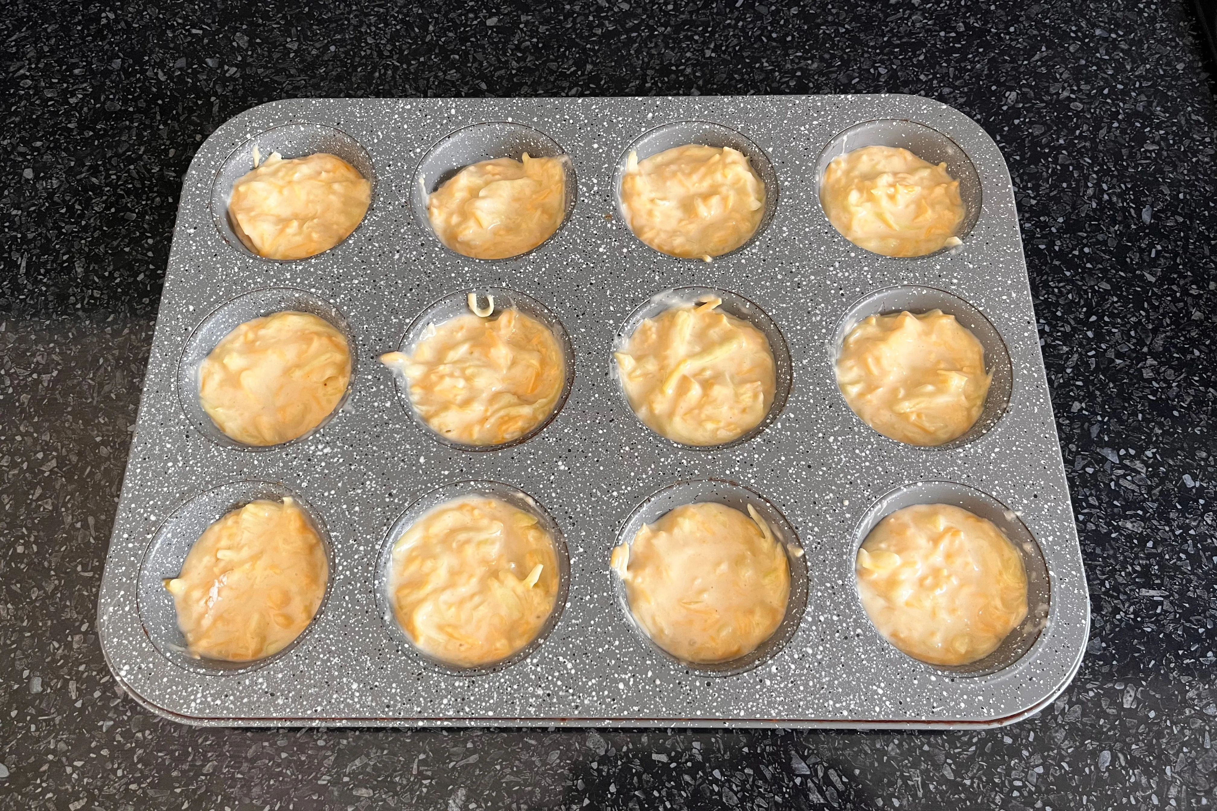 Zucchini and Cheddar batter divided among the wells of a muffin tin