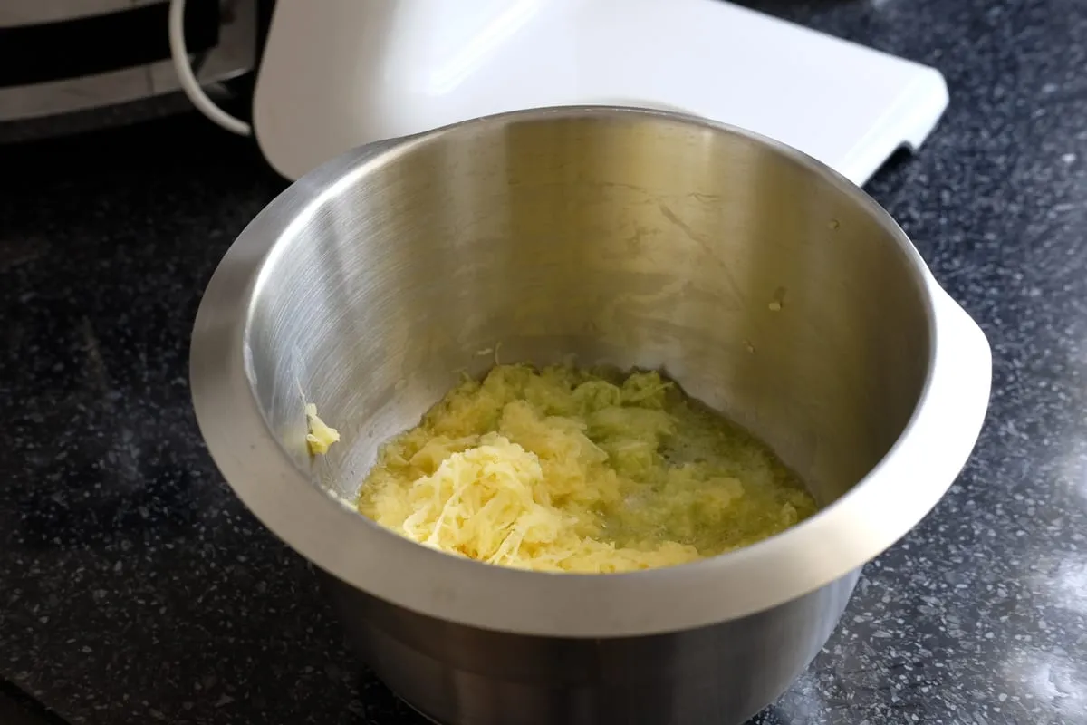 Finely grated potatoes and zucchini with their released juices in a metal bowl