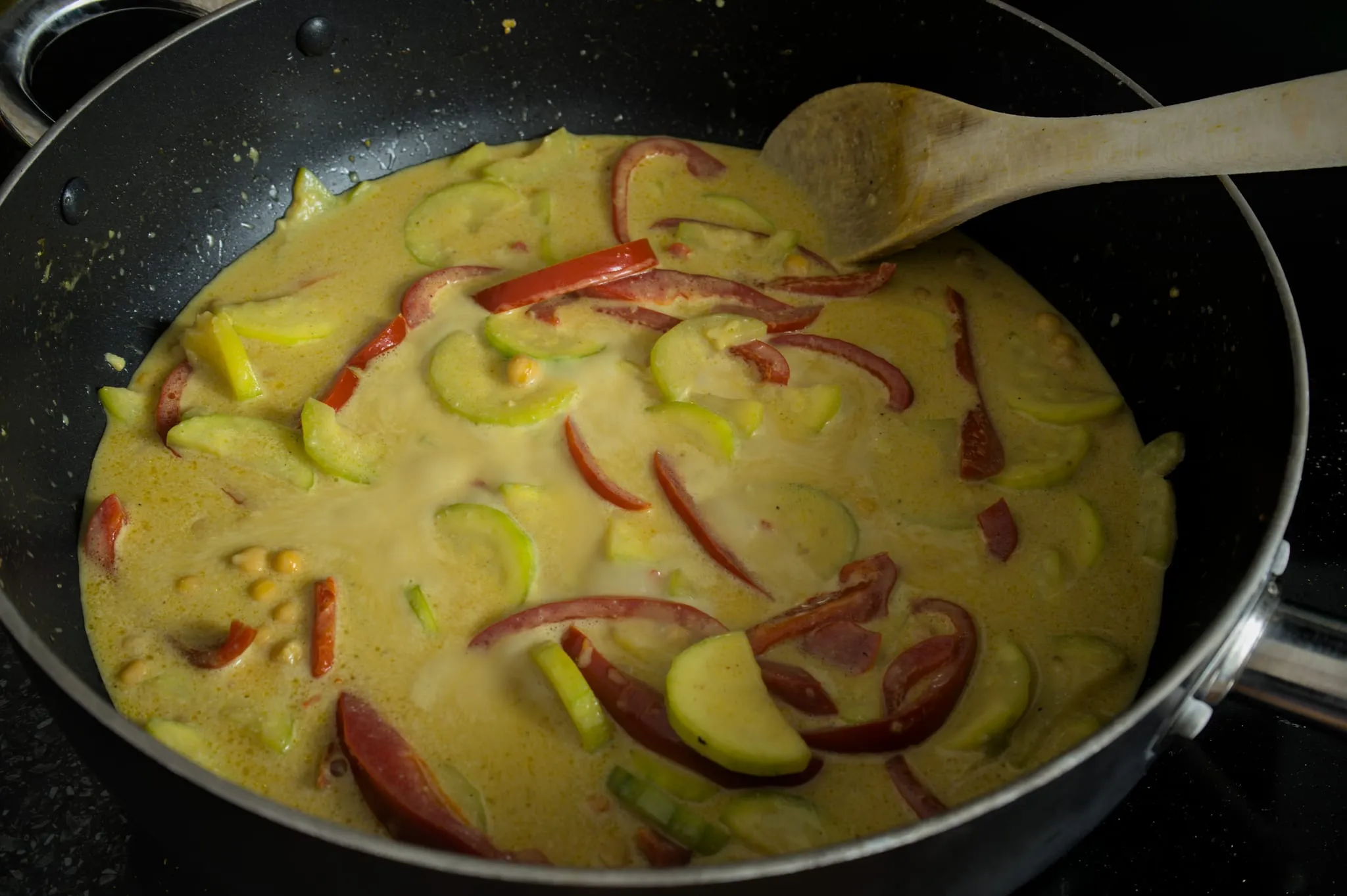 Vegetarian coconut curry with zucchini, red pepper and chickpeas simmering gently in a wide pan
