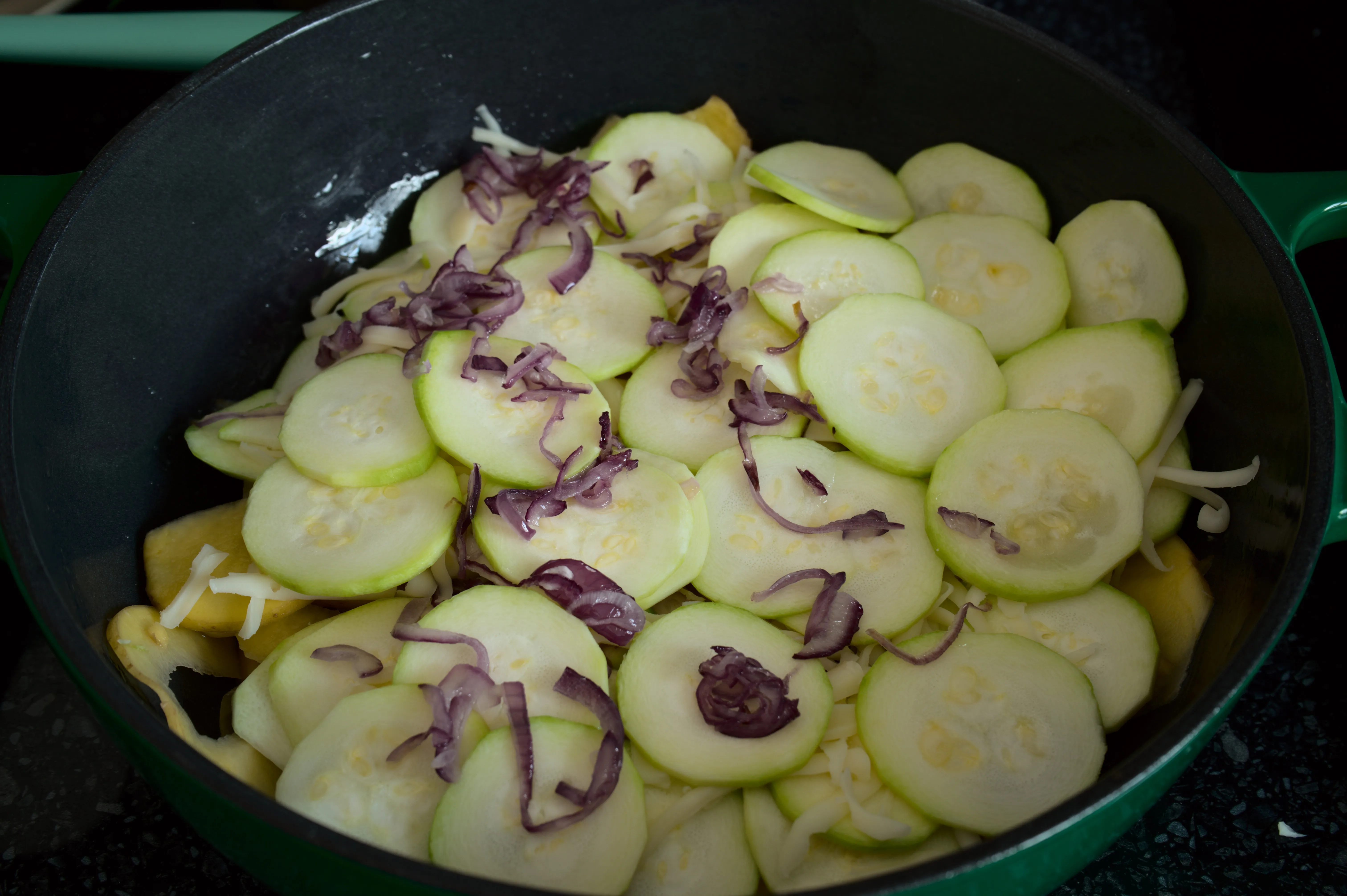 Potato, zucchini, onion and cheese layers assembled in an ovenproof dish before baking