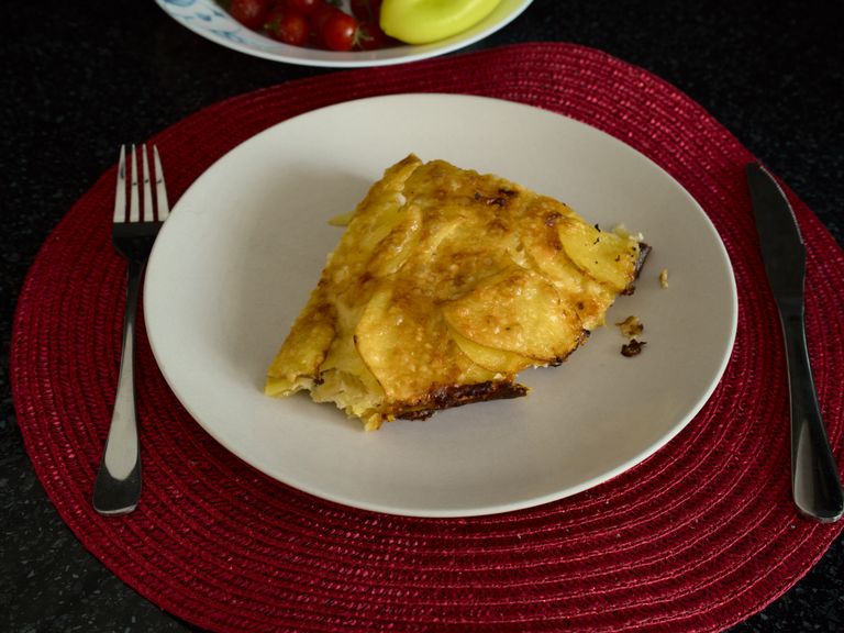 A serving of golden potato and zucchini gratin with Gouda and Parmesan on a white plate