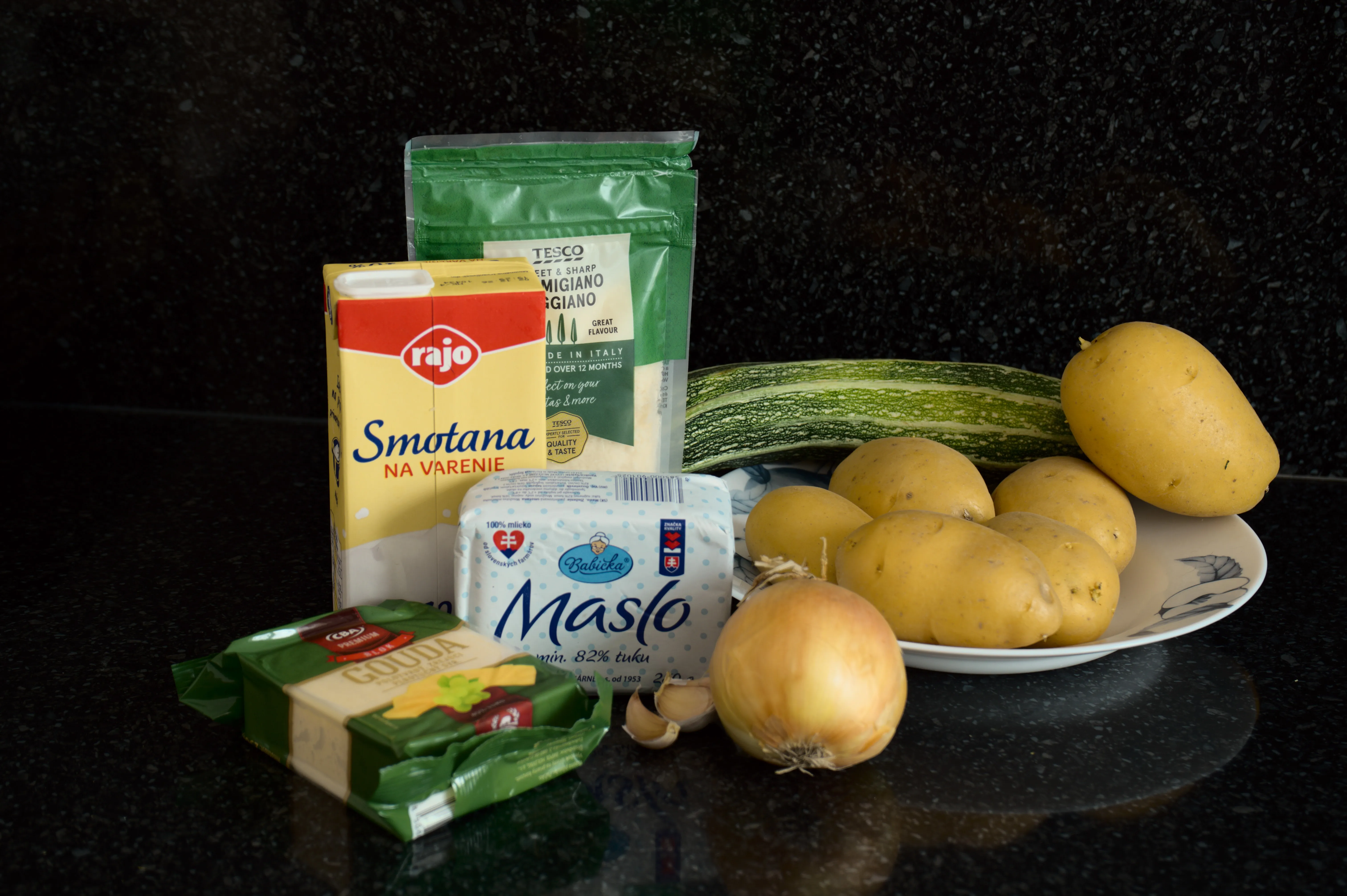 Young potatoes, zucchini, onion, garlic, cream, butter, Gouda and Parmesan prepared for a potato and zucchini gratin