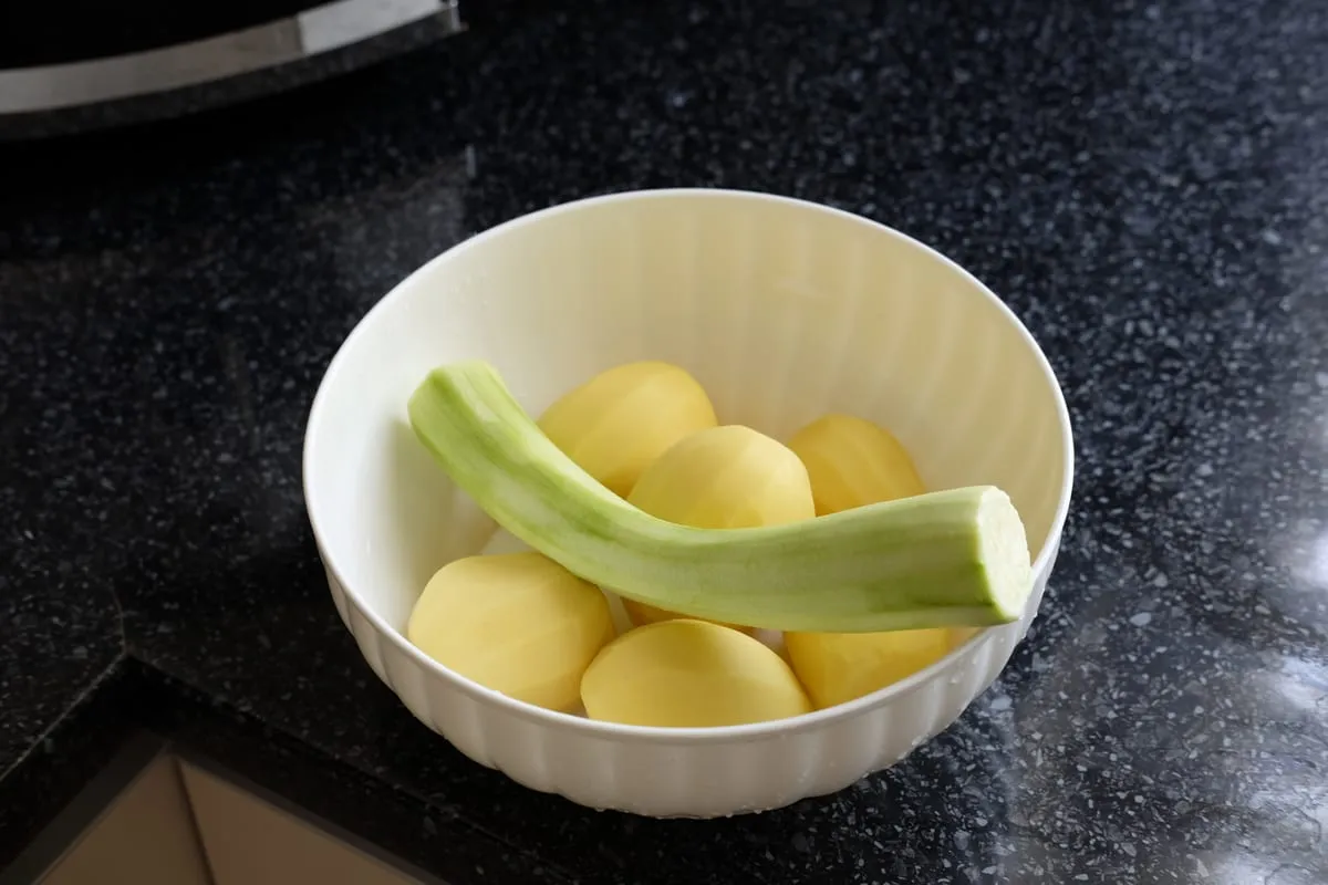 Peeled potatoes and a peeled zucchini prepared in a bowl
