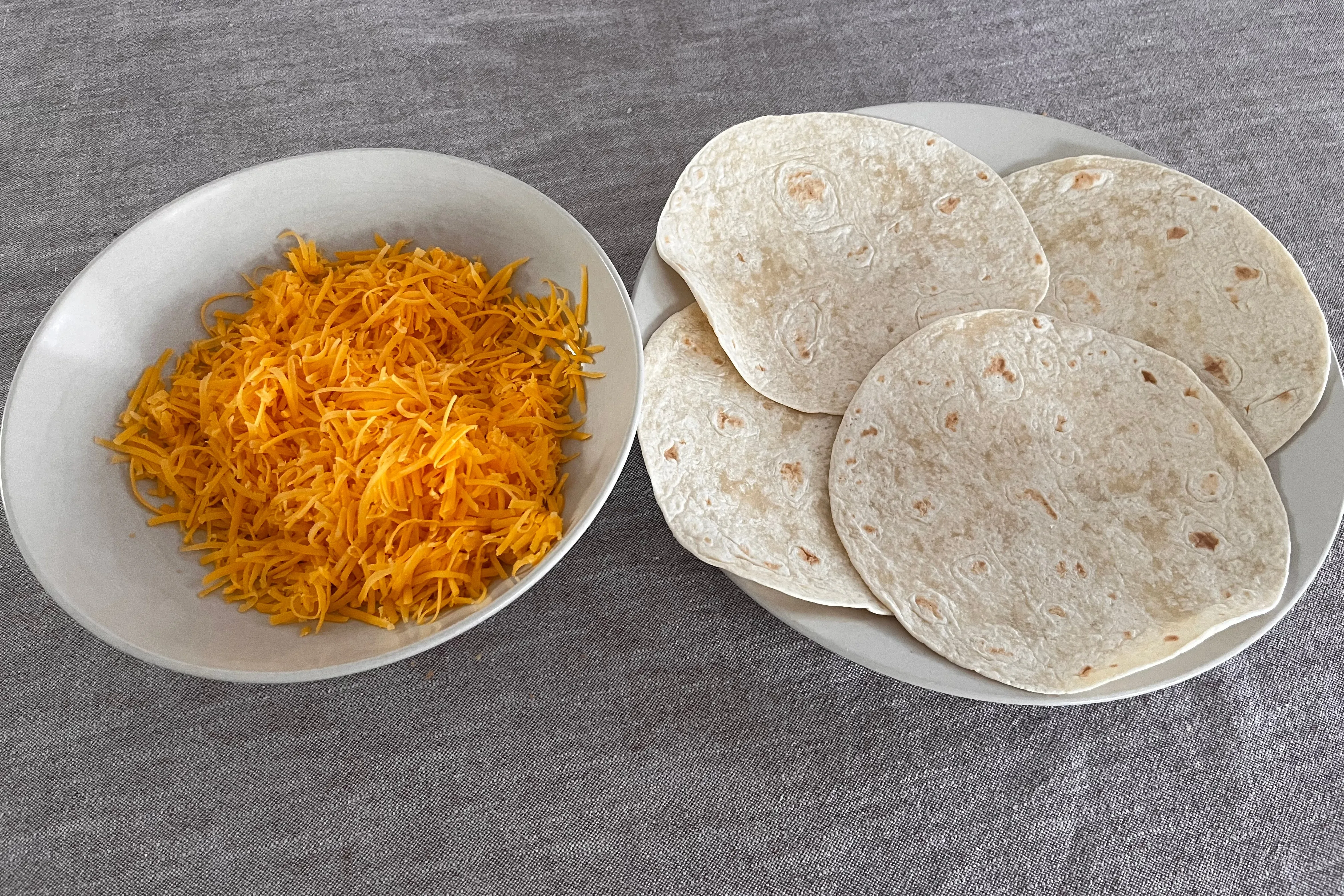 Grated Cheddar beside small wheat-flour tortillas for cheese quesadillas