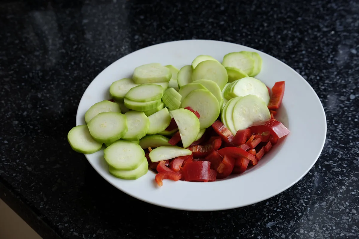 Rounds of peeled zucchini and pieces of red bell pepper prepared on a plate