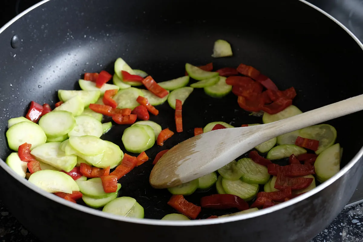 Peeled zucchini and red bell pepper cooking uncovered in a frying pan