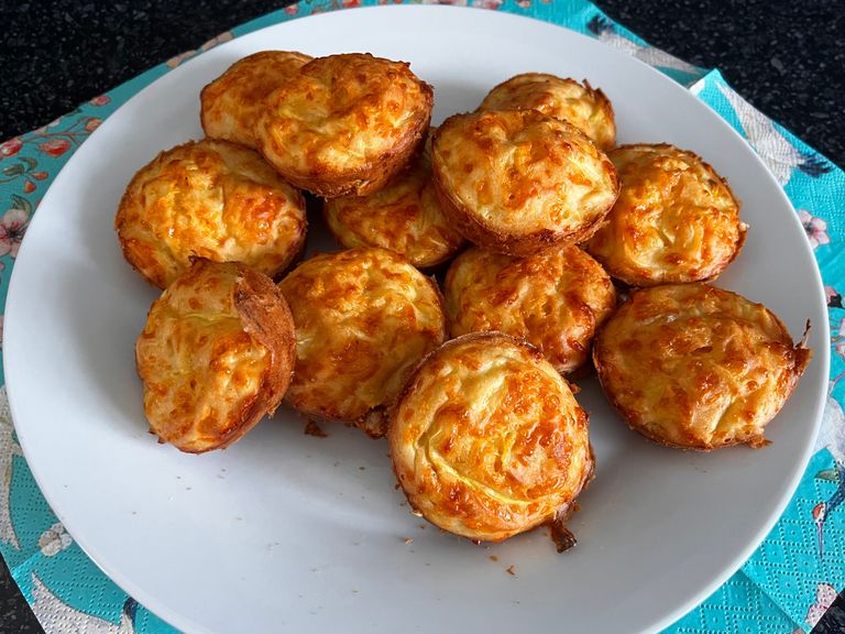 Muffins salados dorados de calabacín y cheddar apilados en un plato blanco