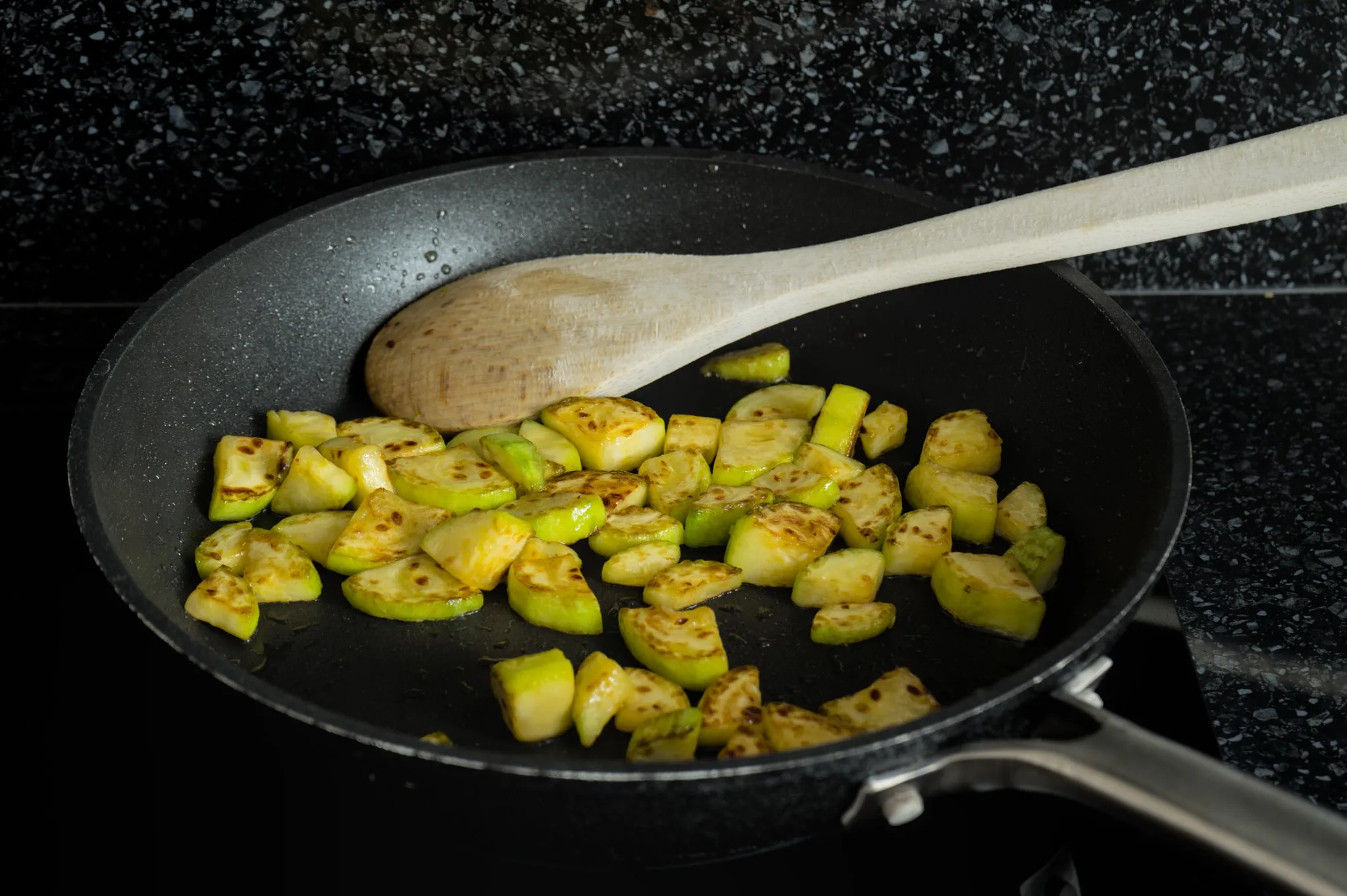 Small pieces of zucchini browning in a frying pan