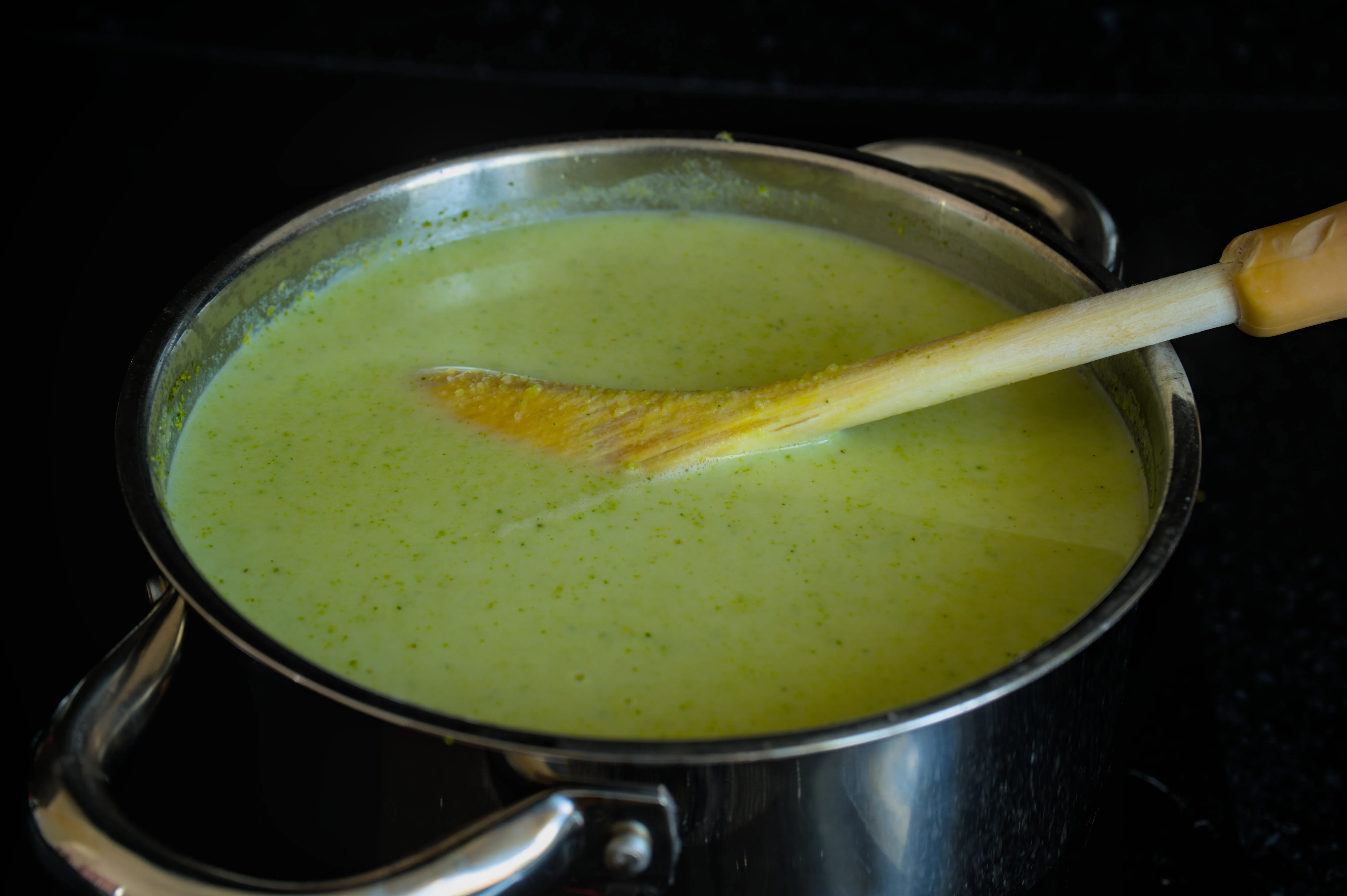 Smooth creamy broccoli soup in a stainless-steel pot with a wooden spoon