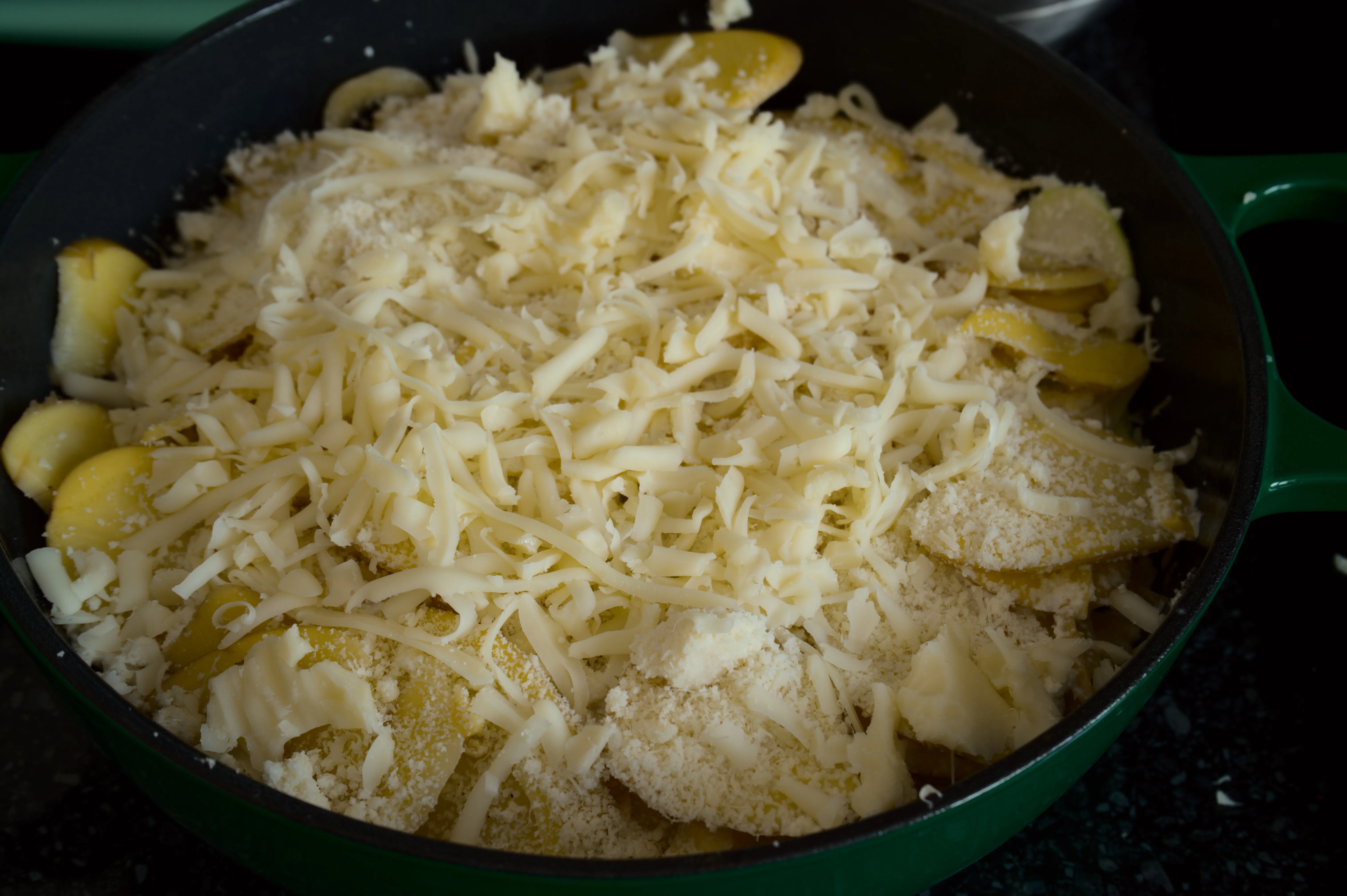 Layered potato and zucchini gratin topped with grated cheese before baking