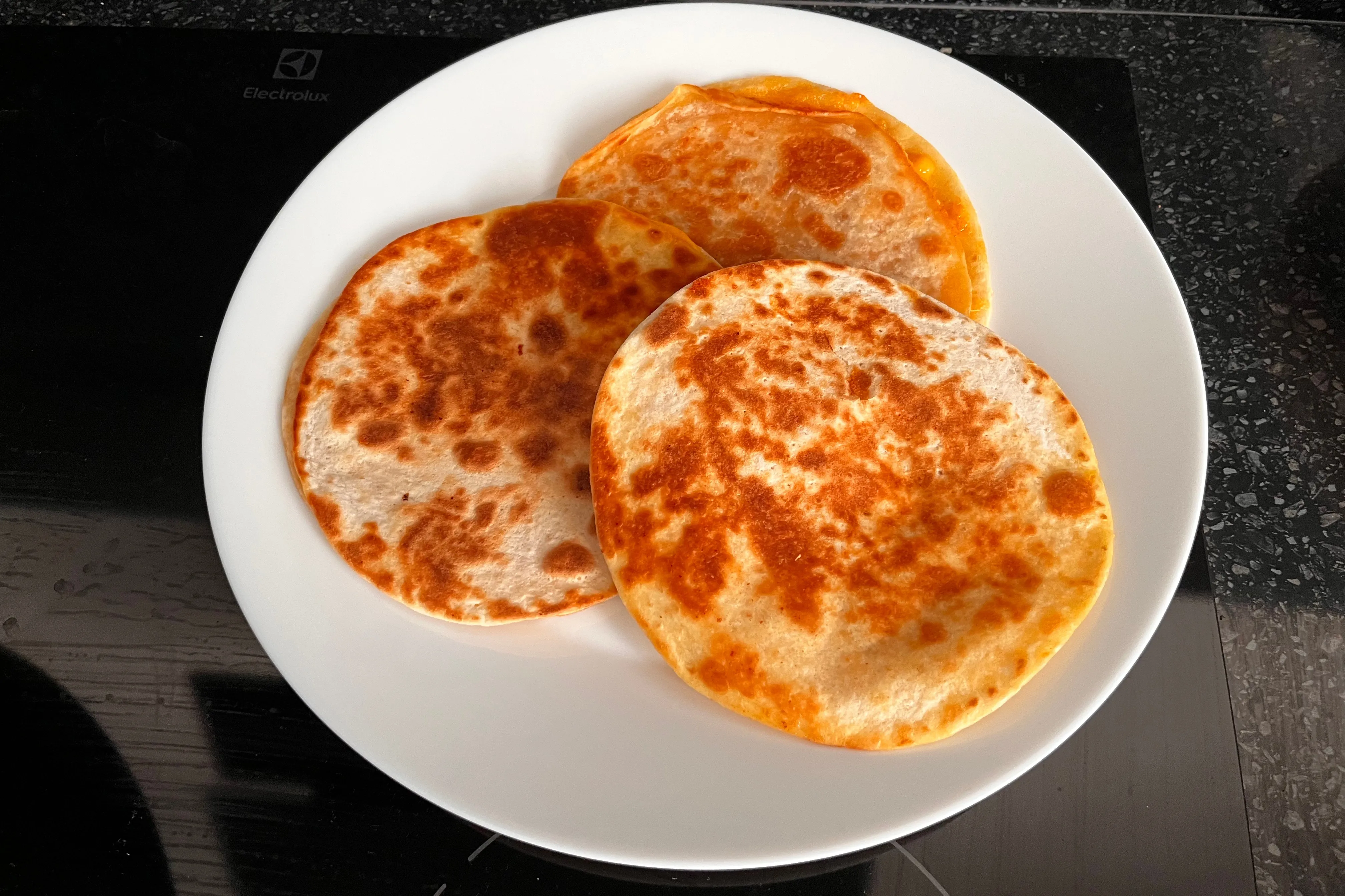 Three whole golden cheese quesadillas on a white plate before slicing