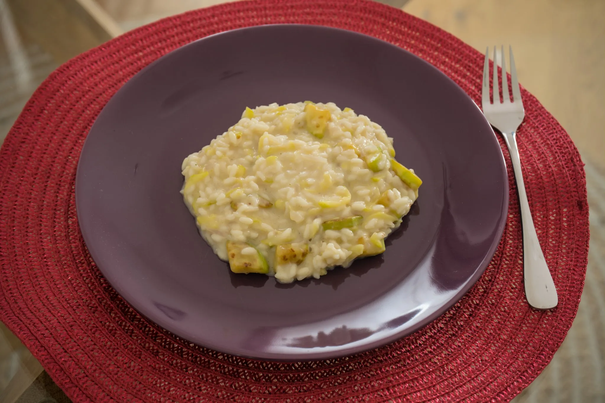 Creamy zucchini risotto with Parmesan on a purple plate and red placemat