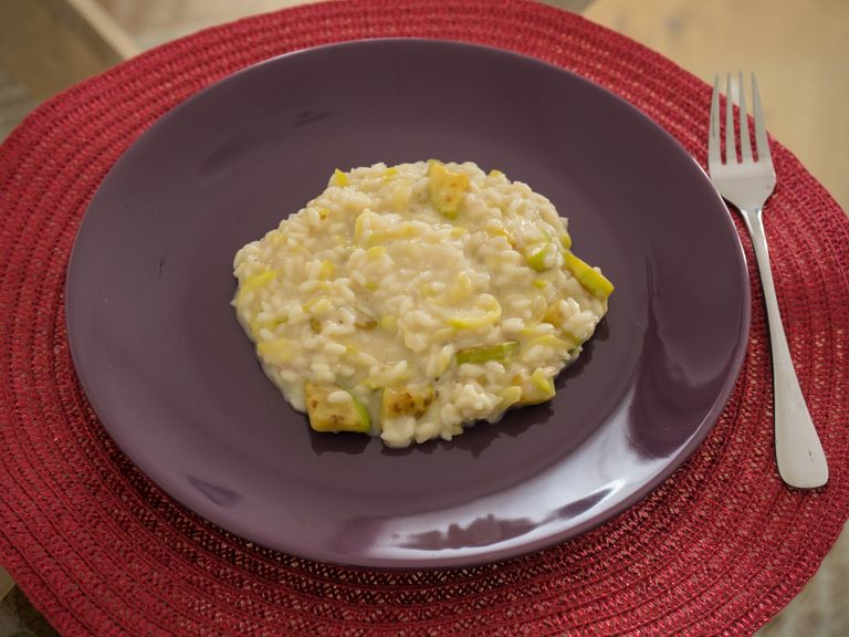 Kermainen kesäkurpitsarisotto parmesaanilla violetilla lautasella punaisen pöytätabletin päällä